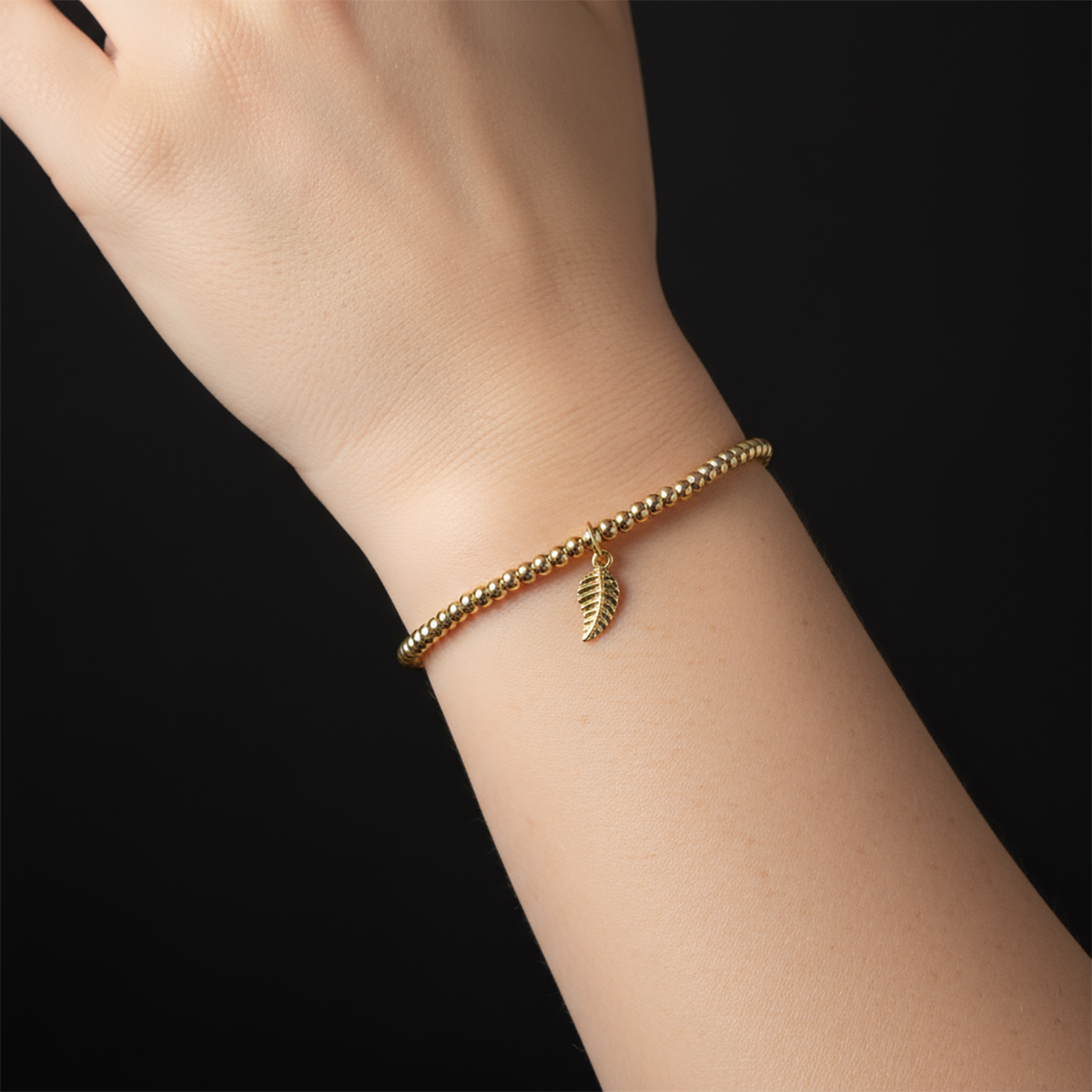 Gold bracelet with a leaf charm on a wrist against a black background