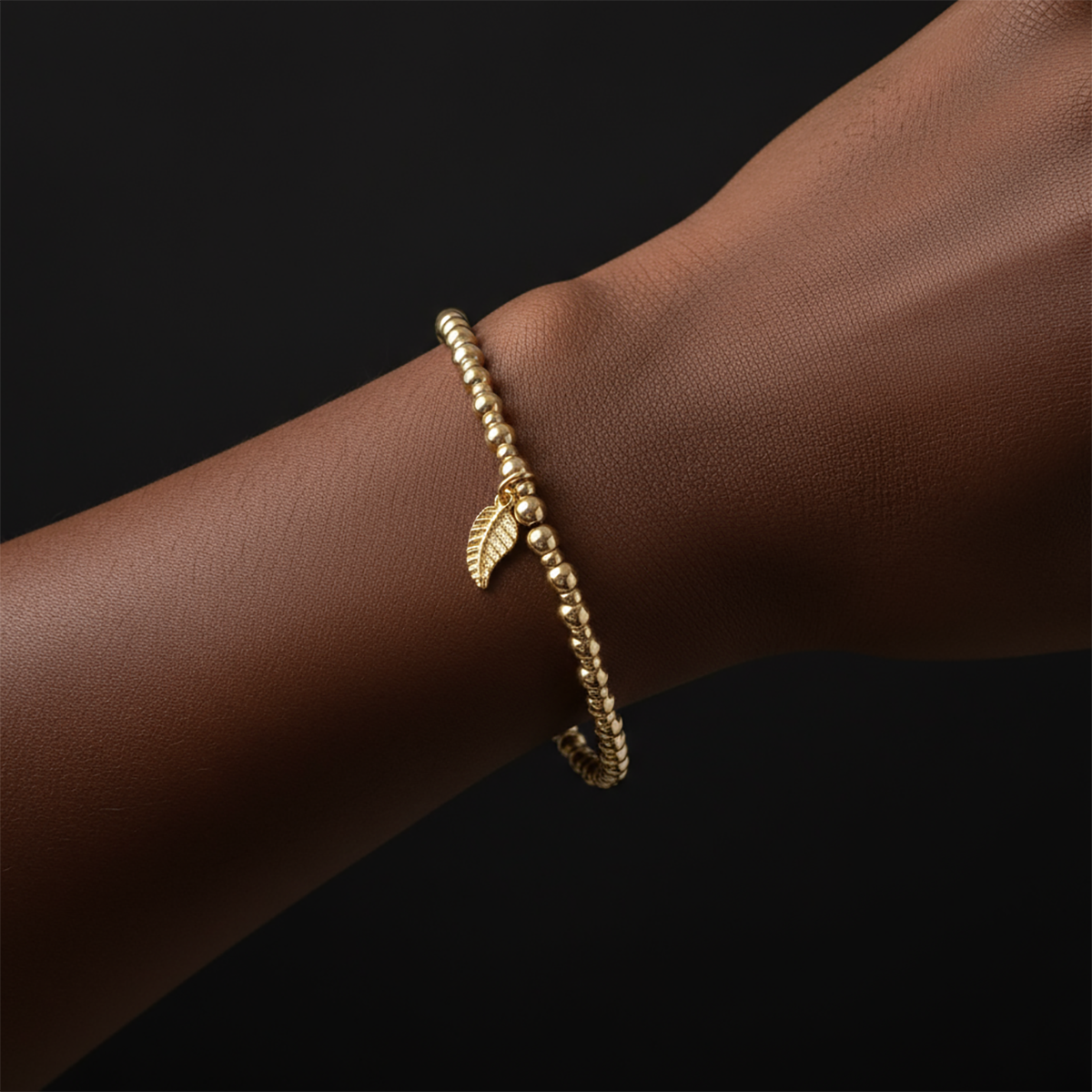 Gold bracelet with a leaf charm on a wrist against a black background