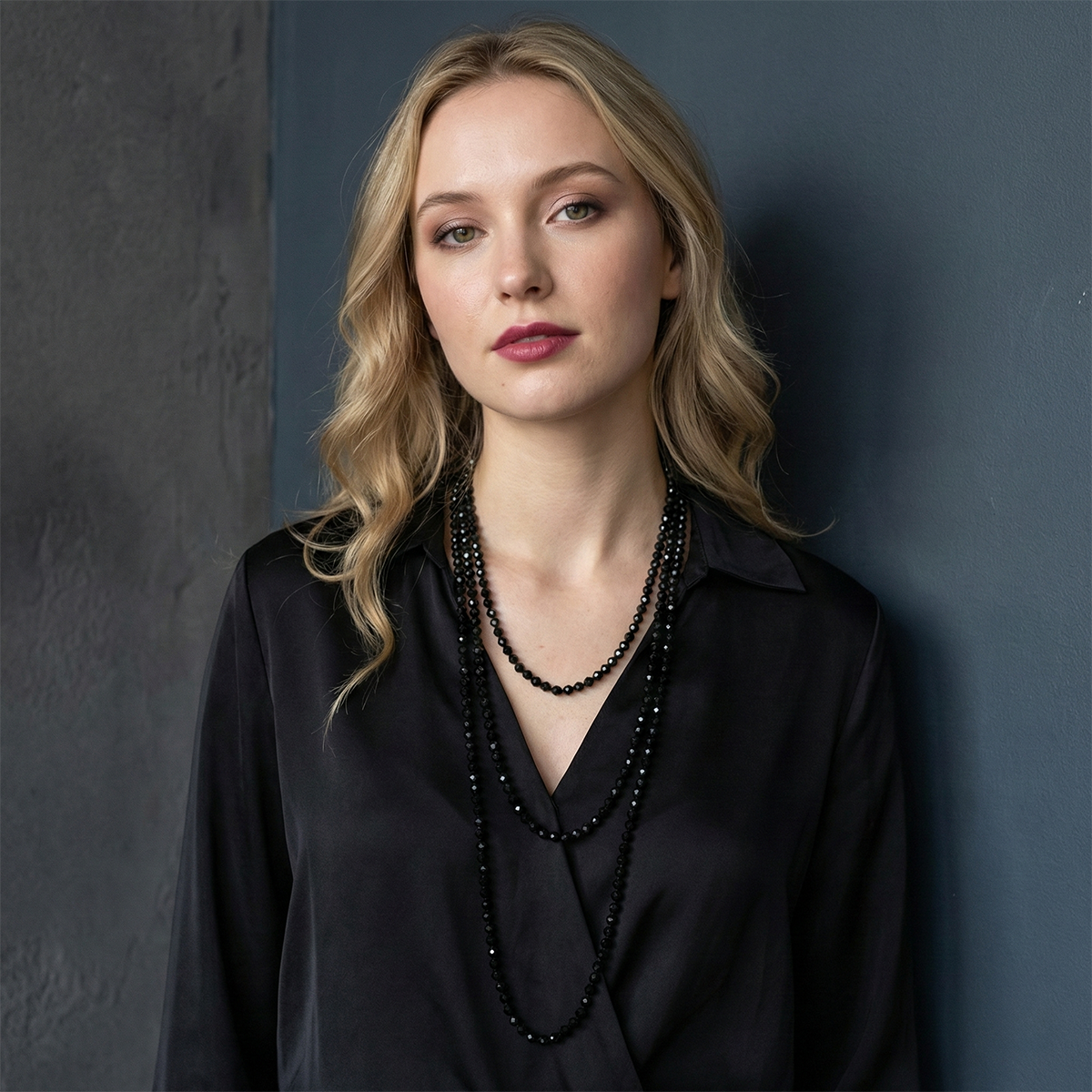 Woman wearing a black blouse and multiple necklaces against a dark background
