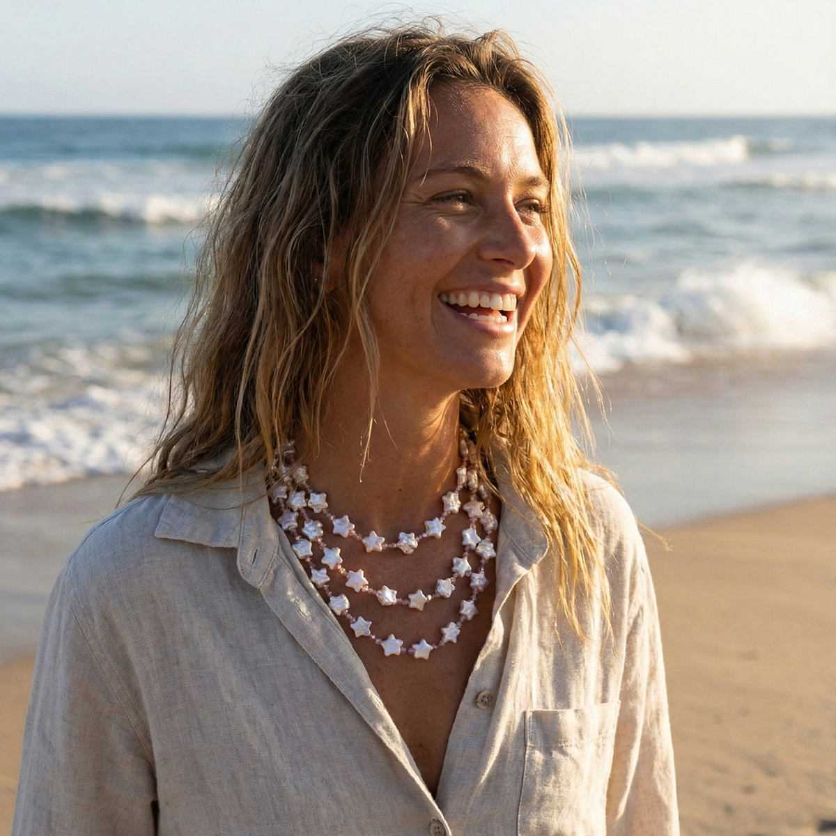 Woman standing on a beach wearing a star-shaped necklace with ocean waves in the background