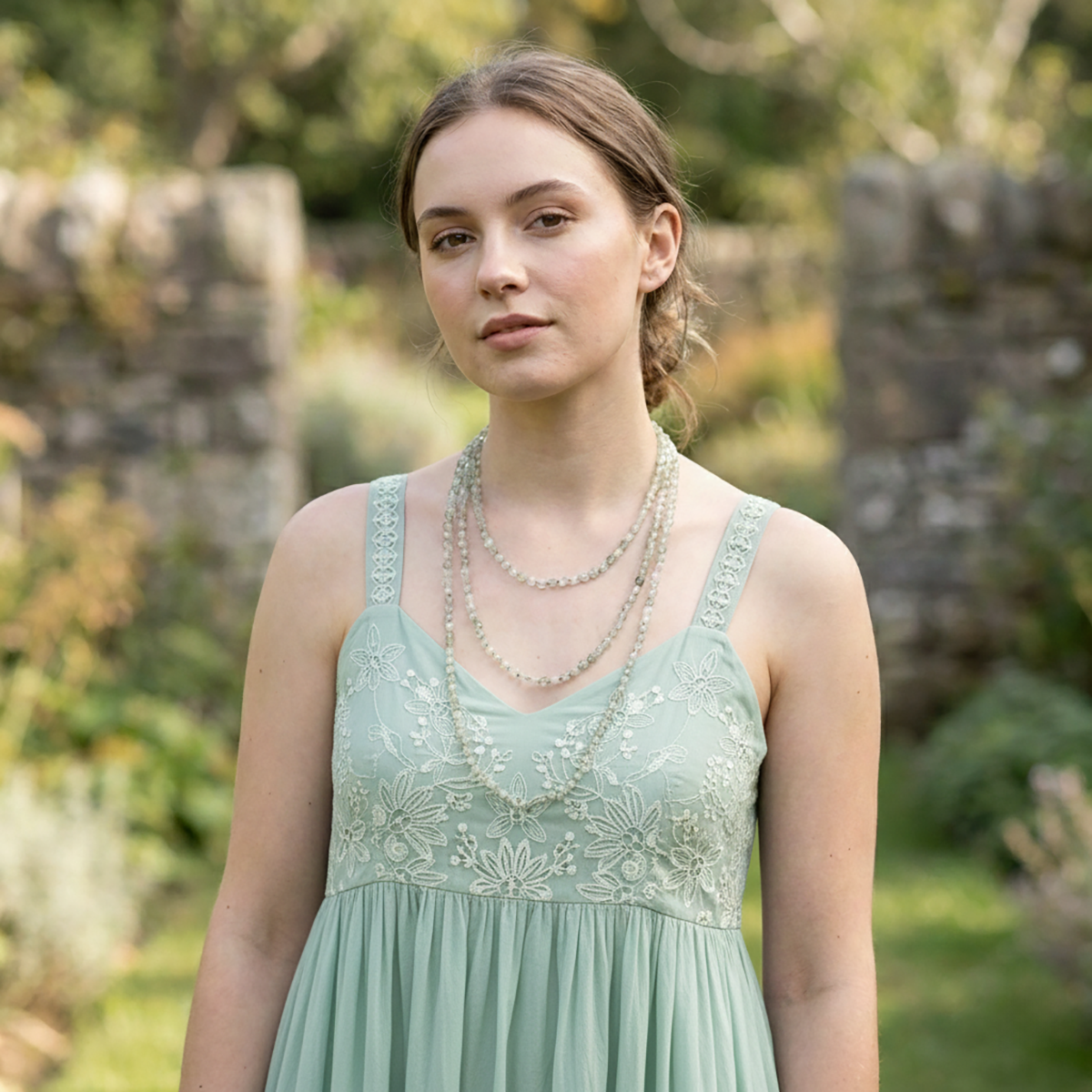 Woman in a light green dress with embroidery standing outdoors in a garden.