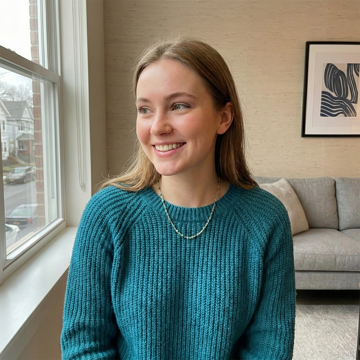 Woman in a teal sweater standing by a window in a living room.