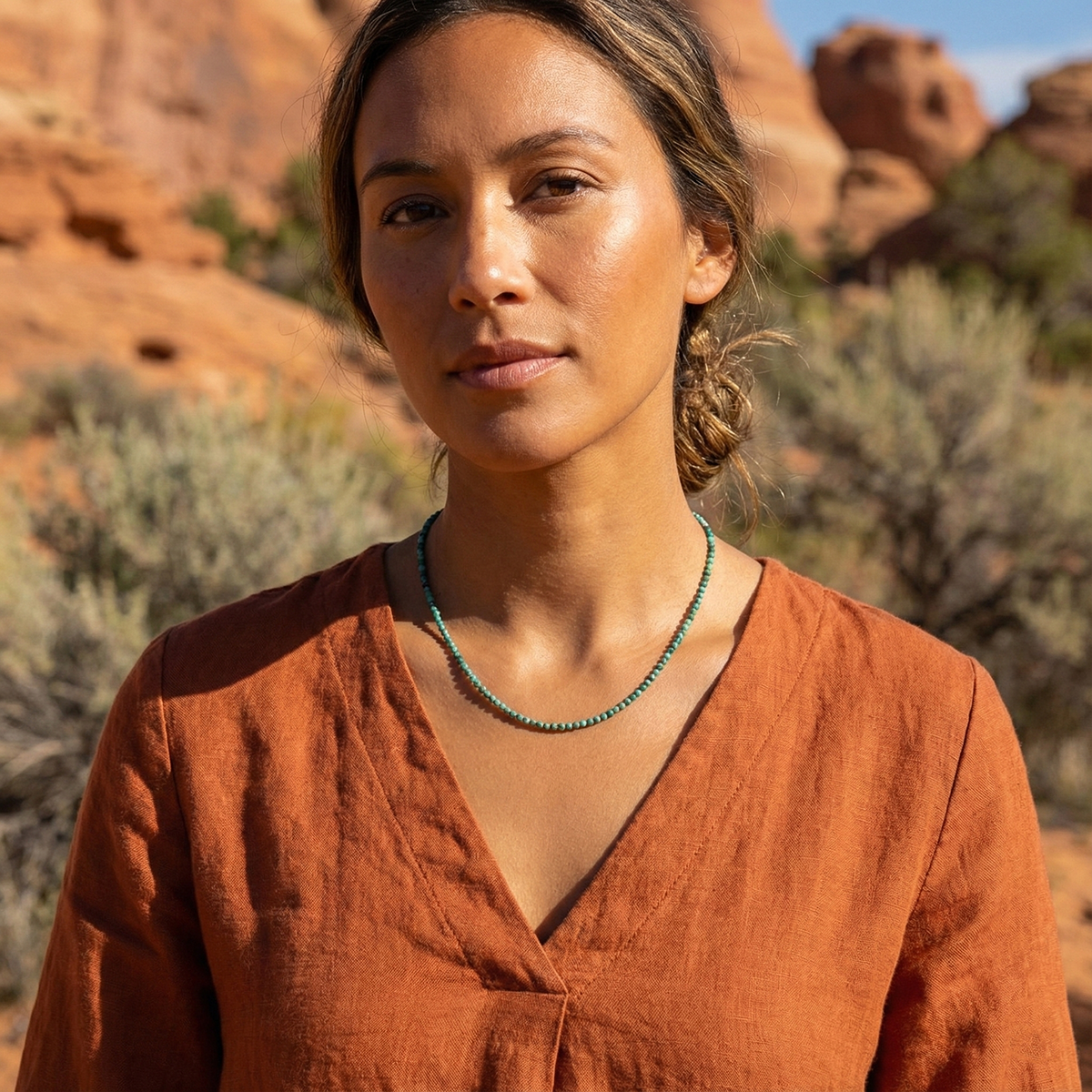 Woman in an orange top with a necklace standing in a desert landscape