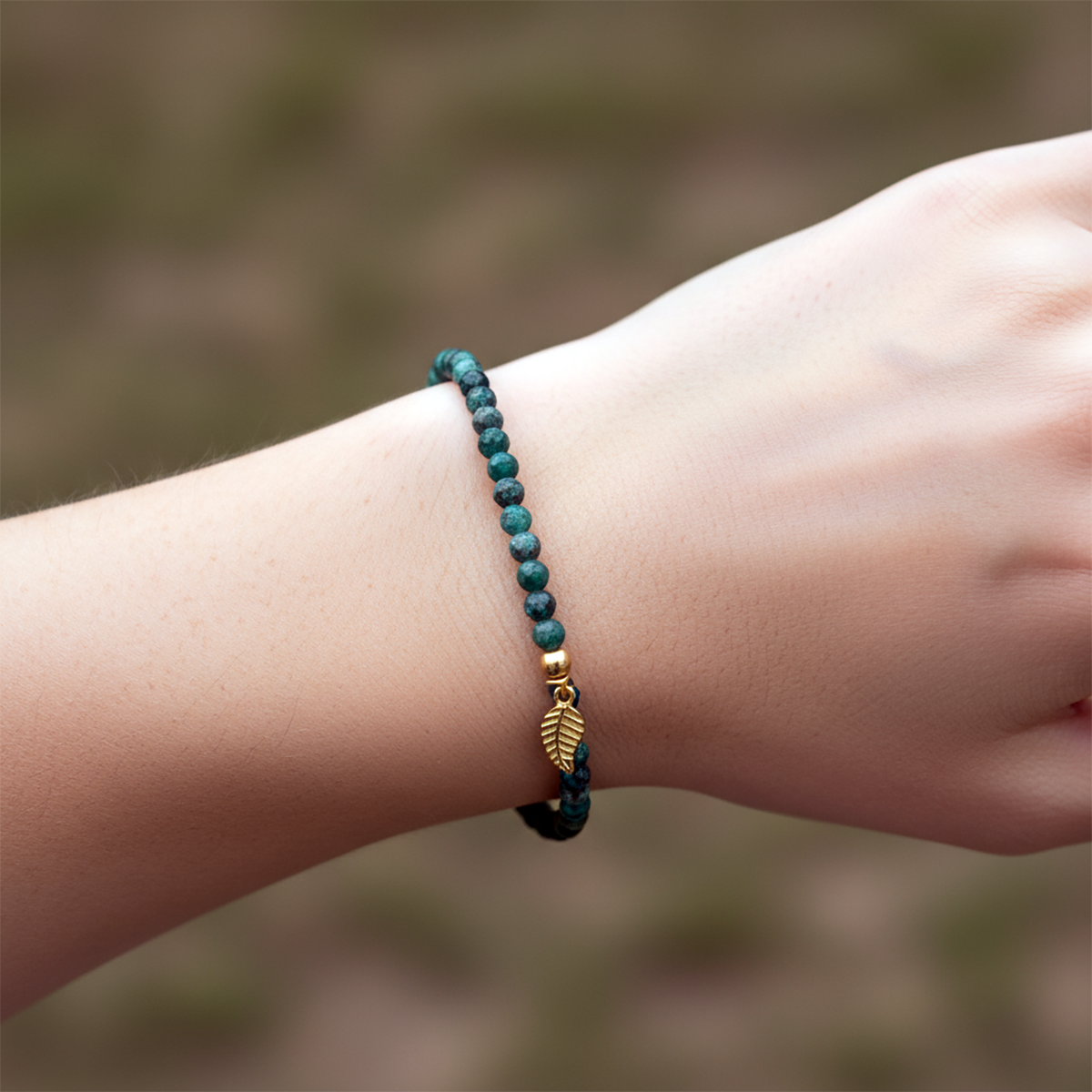 Green beaded bracelet with a gold leaf charm on a wrist against a blurred natural background