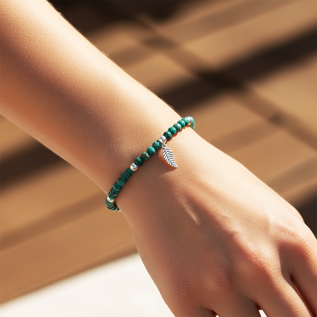 Green beaded bracelet with a leaf charm on a wrist against a blurred background