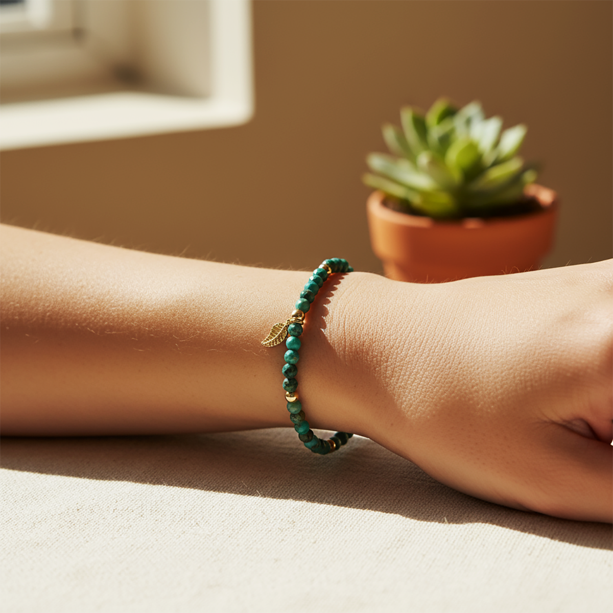 Green beaded bracelet on a wrist with a potted succulent in the background