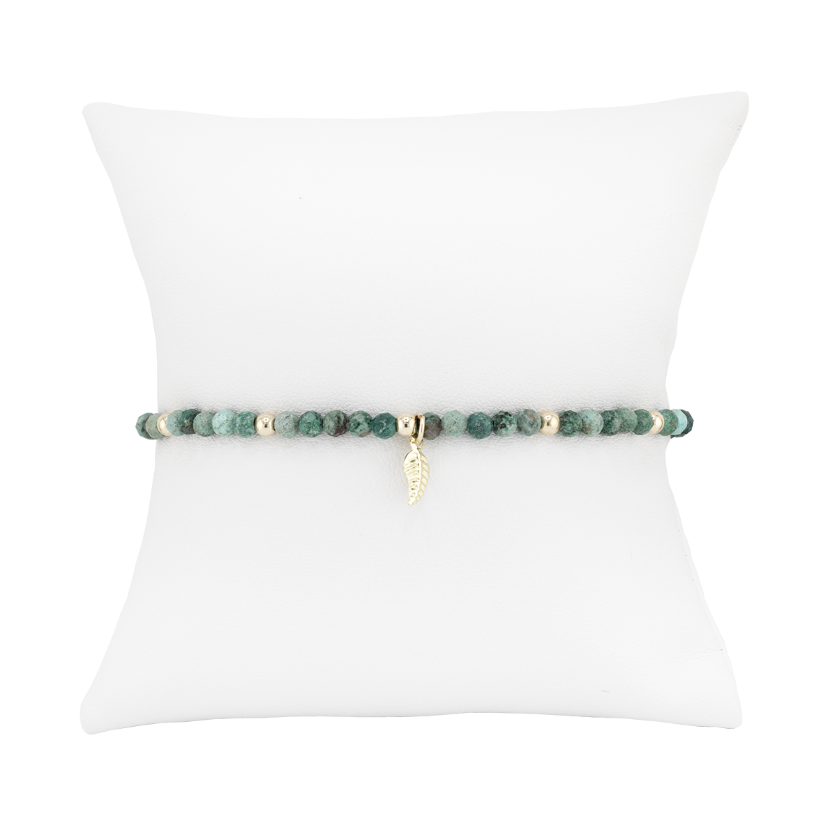 Green beaded bracelet with a gold charm on a white pillow