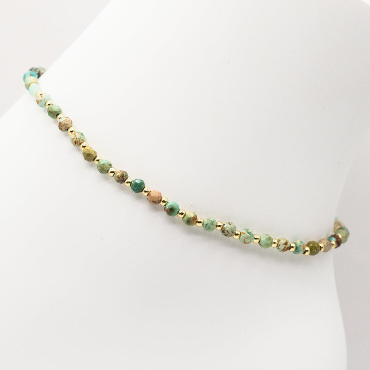 Beaded anklet with green and gold beads on a white background