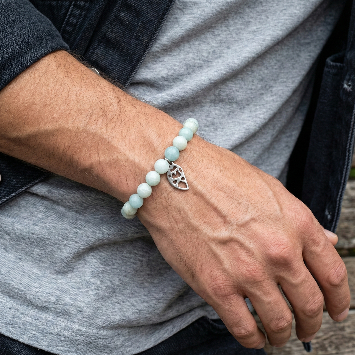 Close-up of a wrist wearing a bracelet with a silver leaf charm, against a neutral background.