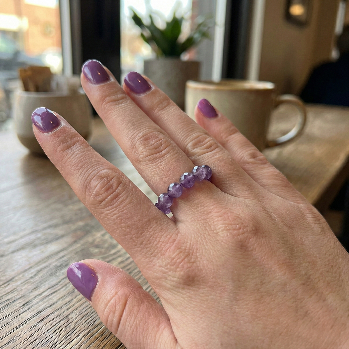 Hand wearing a purple beaded ring with a blurred cafe background