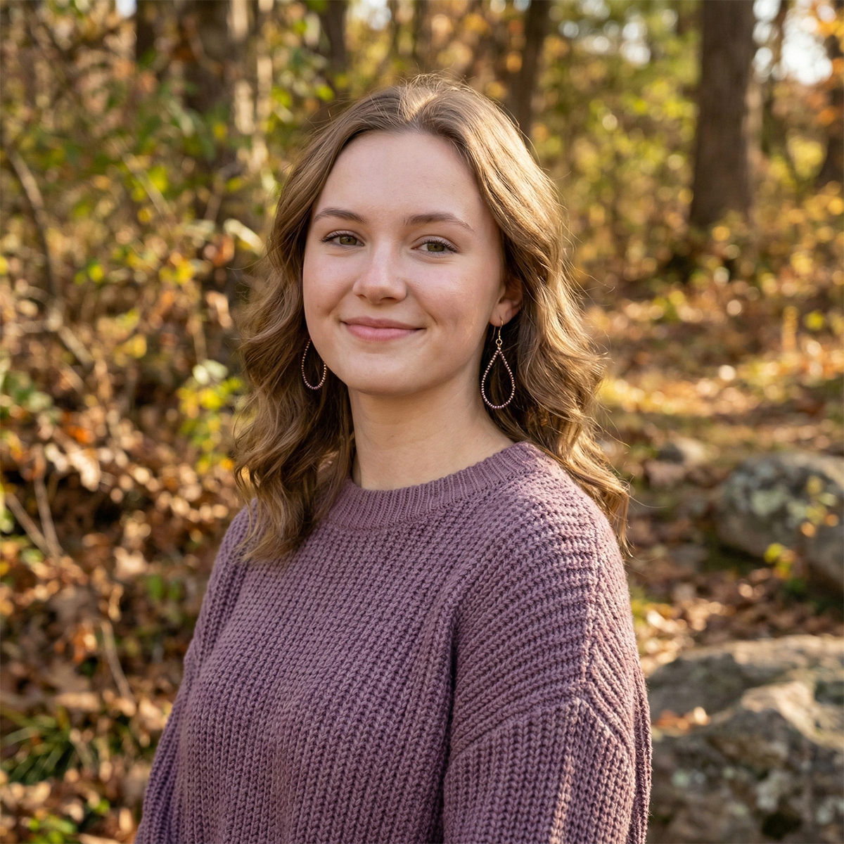 Woman in a purple sweater standing in a forest with autumn foliage