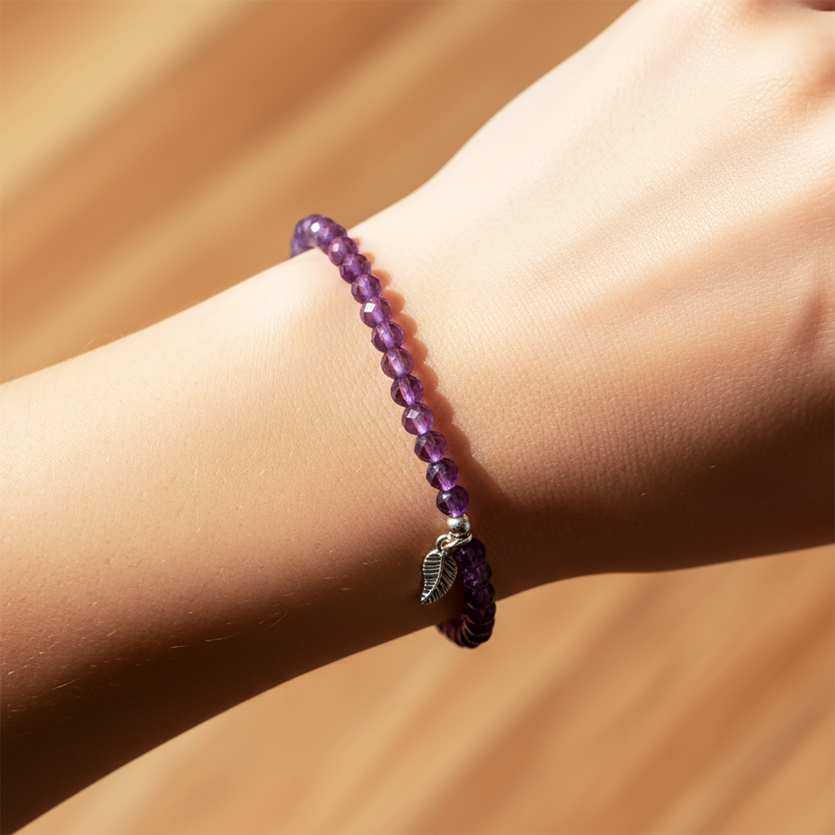 Purple beaded bracelet with a leaf charm on a wrist against a beige background