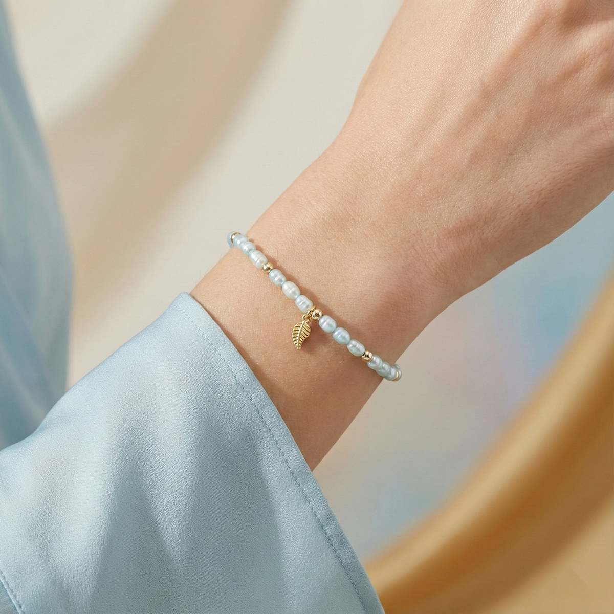 Pearl bracelet with a gold leaf charm on a wrist against a neutral background