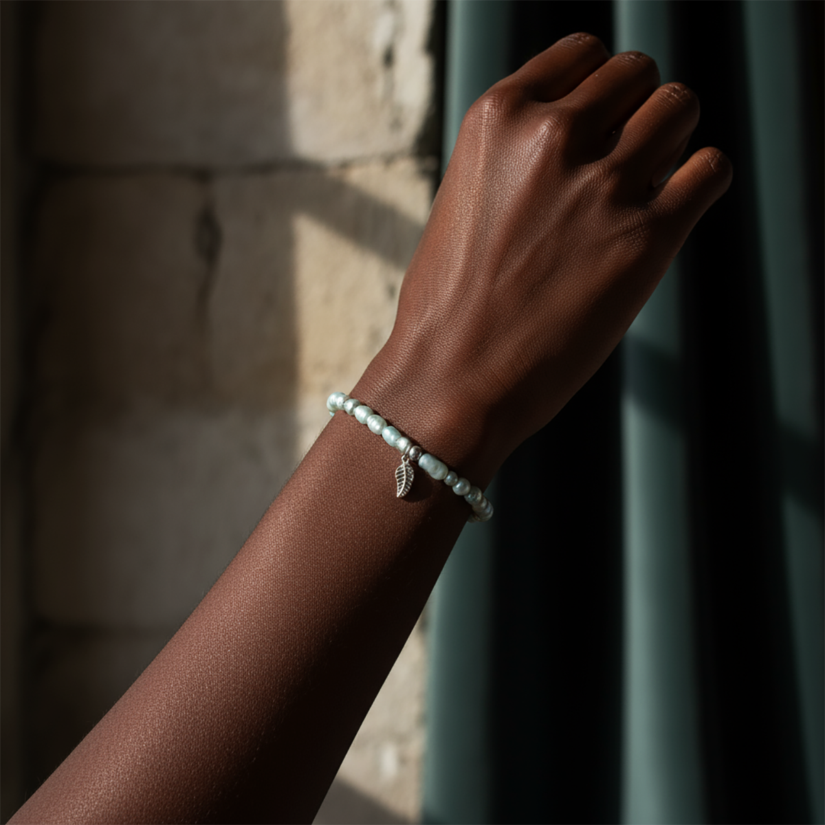 Hand wearing a bracelet with a leaf charm against a textured wall.