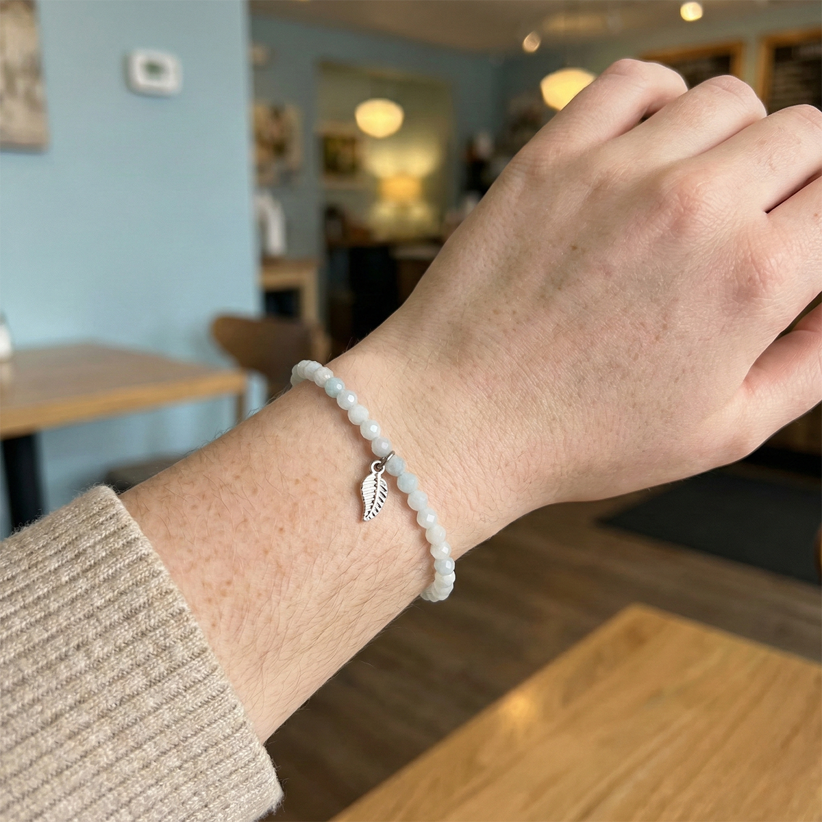 Hand wearing a bracelet with a leaf charm in an indoor setting