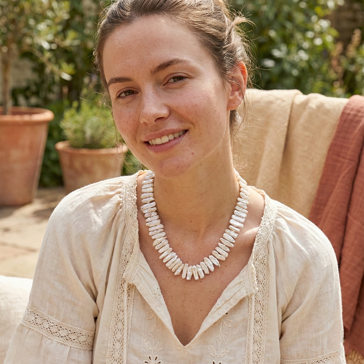 Woman wearing a white necklace outdoors with plants in the background