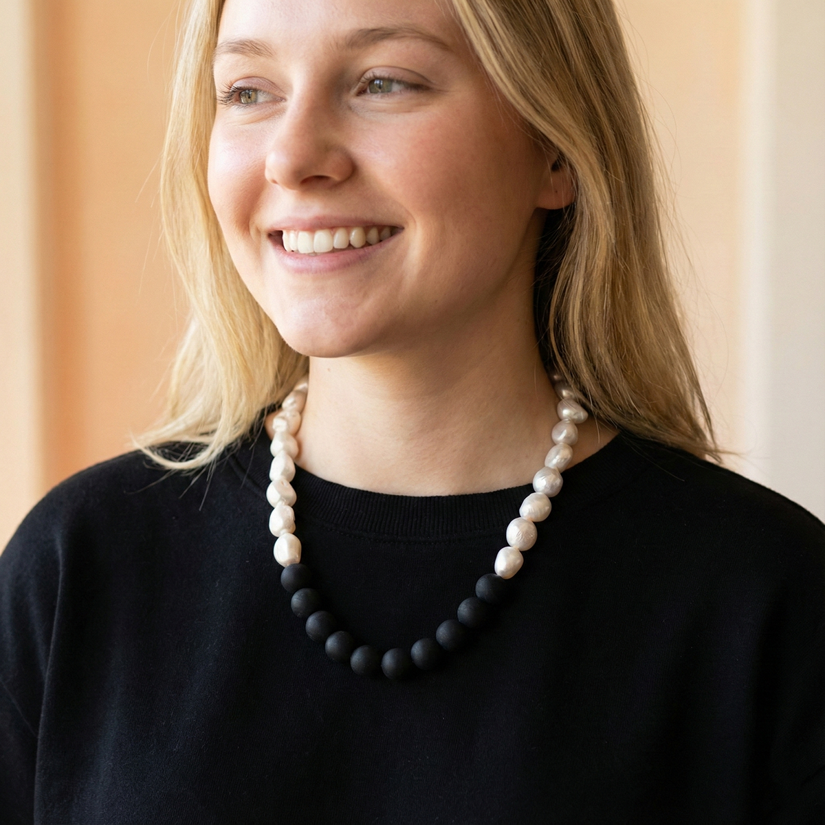 Woman wearing a black and white beaded necklace against a neutral background