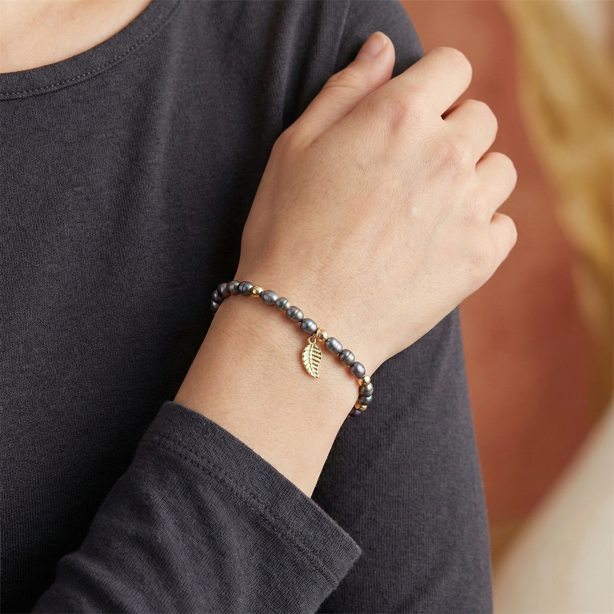 Person wearing a bracelet with a leaf charm on a blurred background