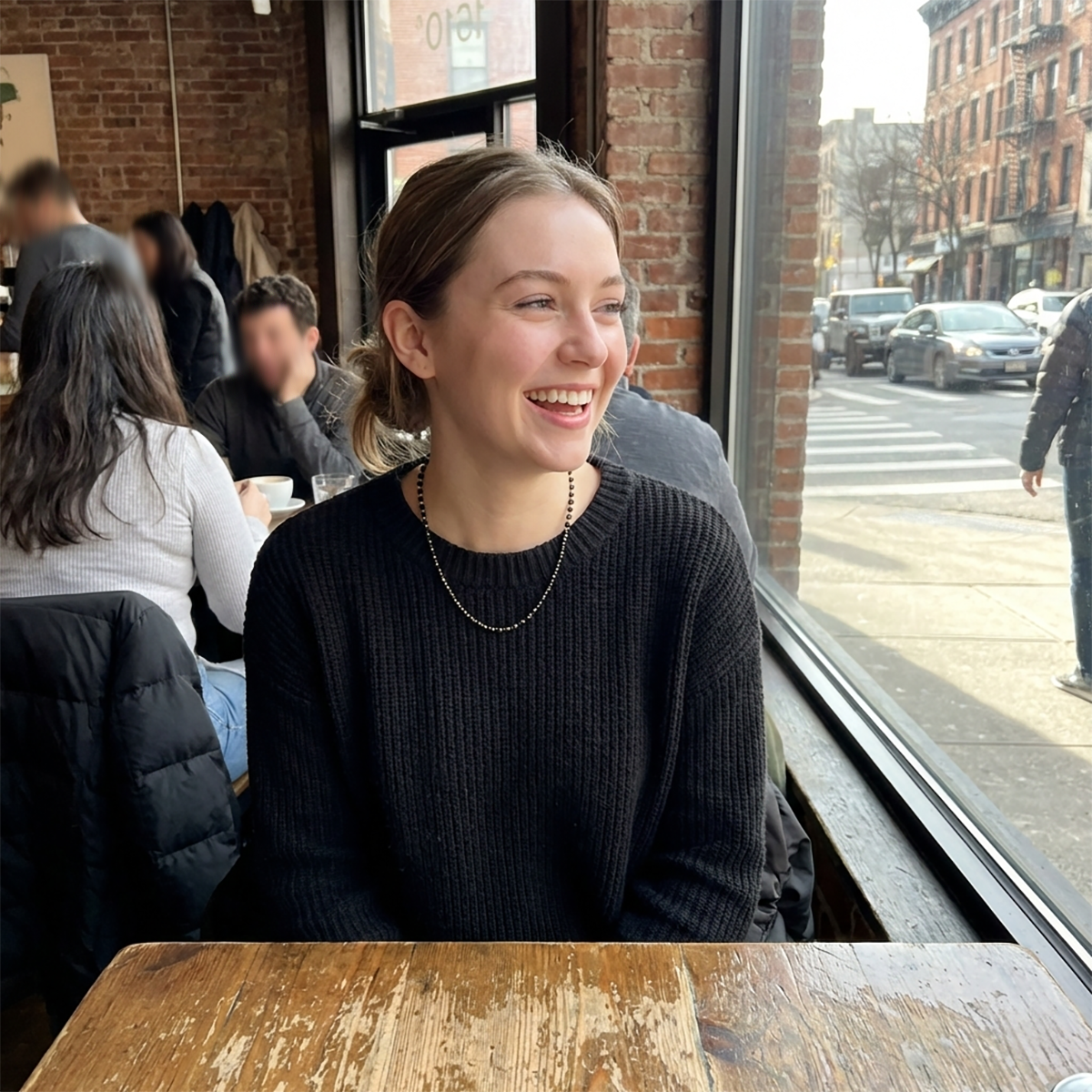 Woman sitting at a table in a cafe with a window view of a street.