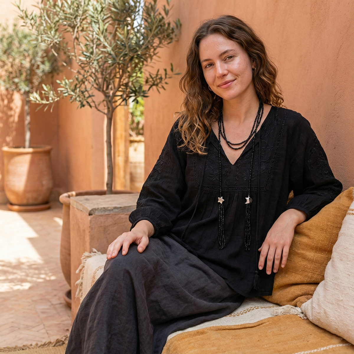 Woman in a black dress sitting on a couch with a warm-toned outdoor setting