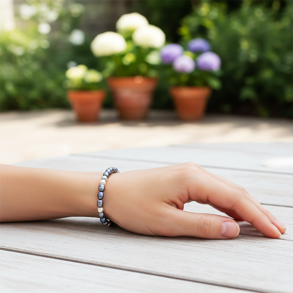 Hand wearing a bracelet on a wooden surface with blurred flowers in the background