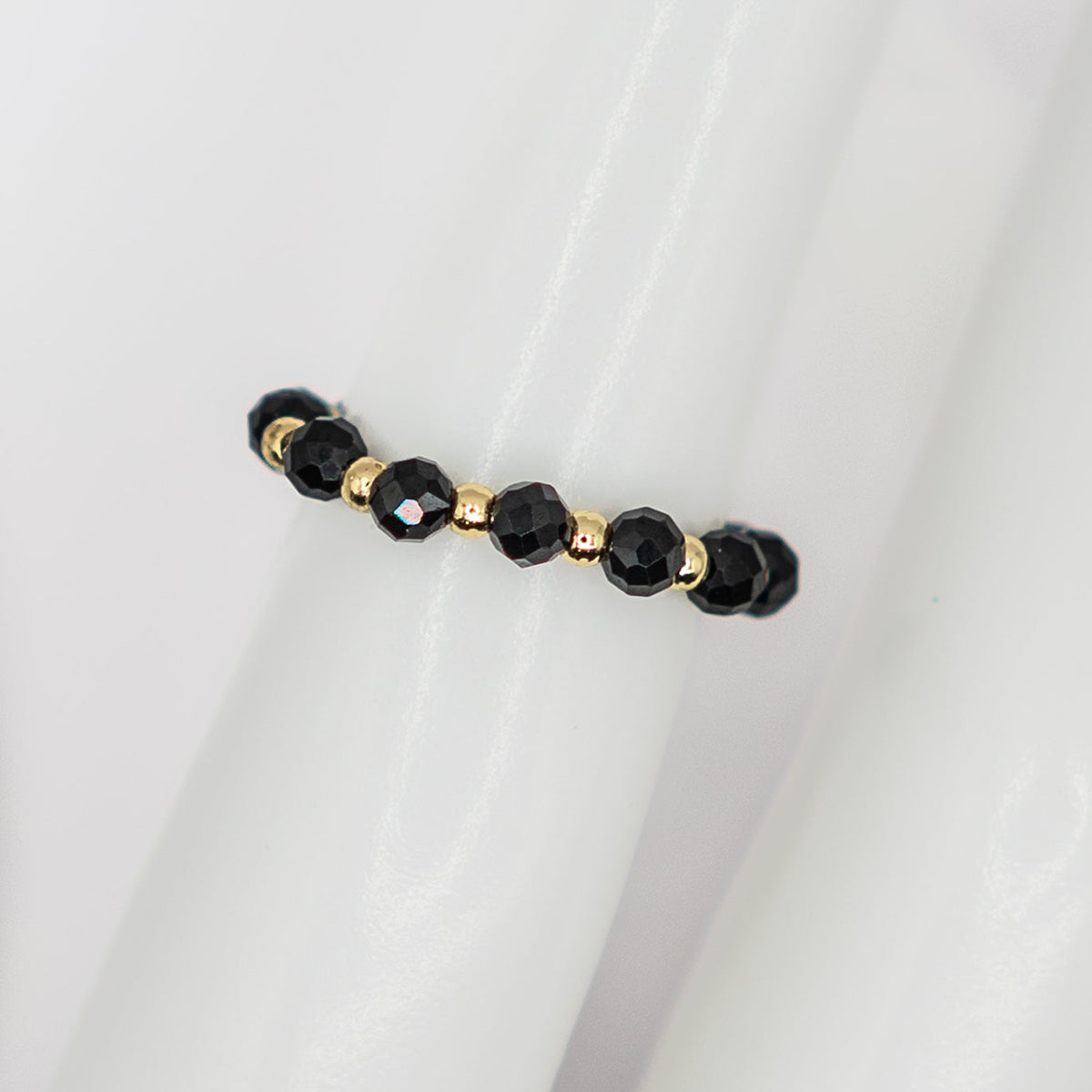 Black beaded bracelet with gold accents on a white fabric background