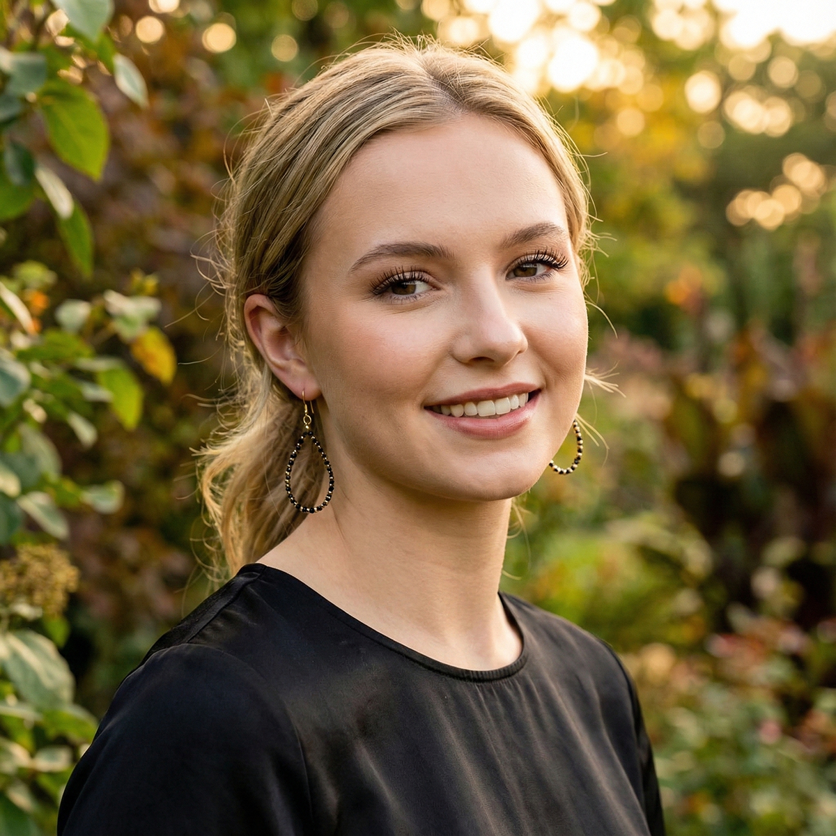 Woman with blonde hair and a black top standing in front of green foliage