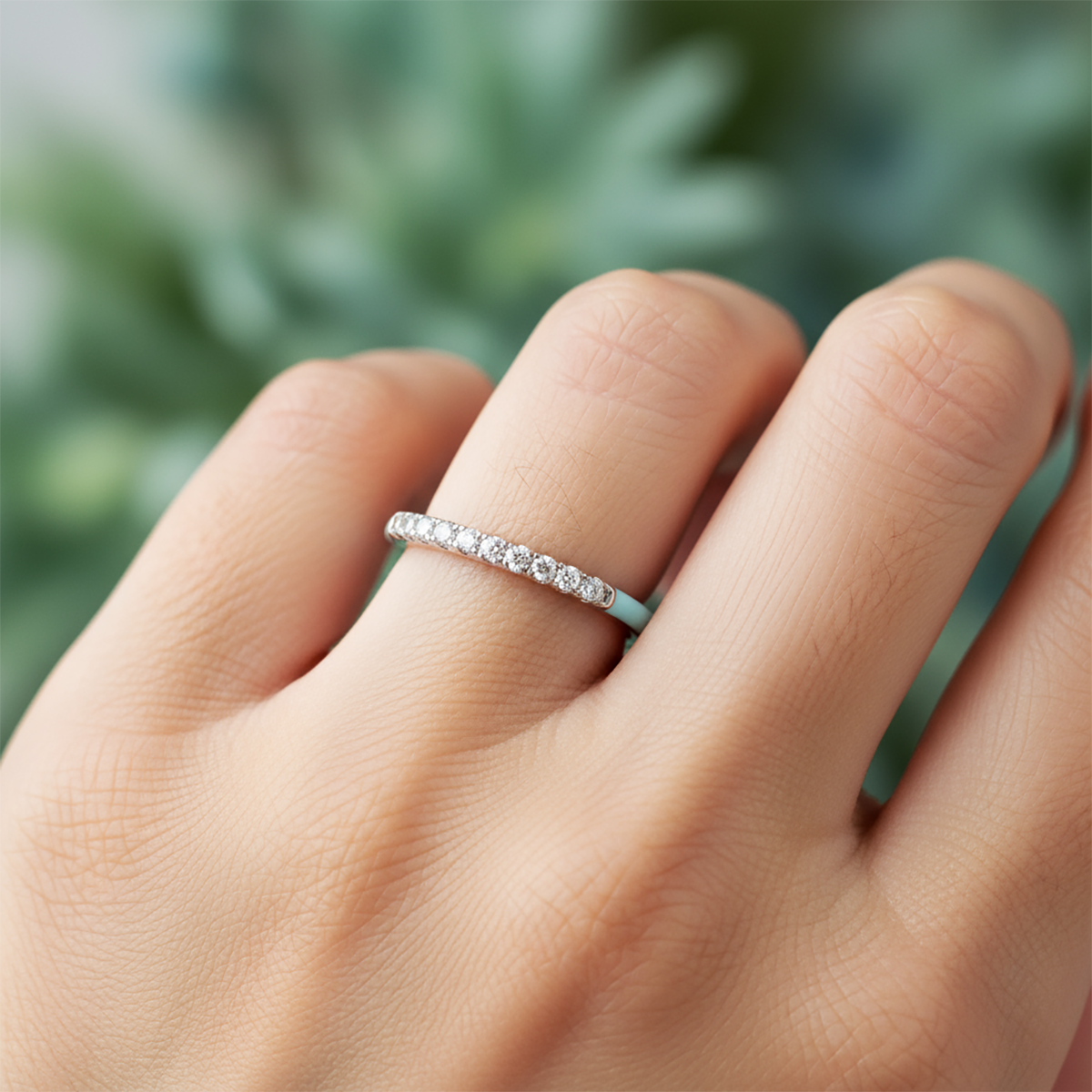 Close-up of a hand wearing a diamond ring with a blurred green background