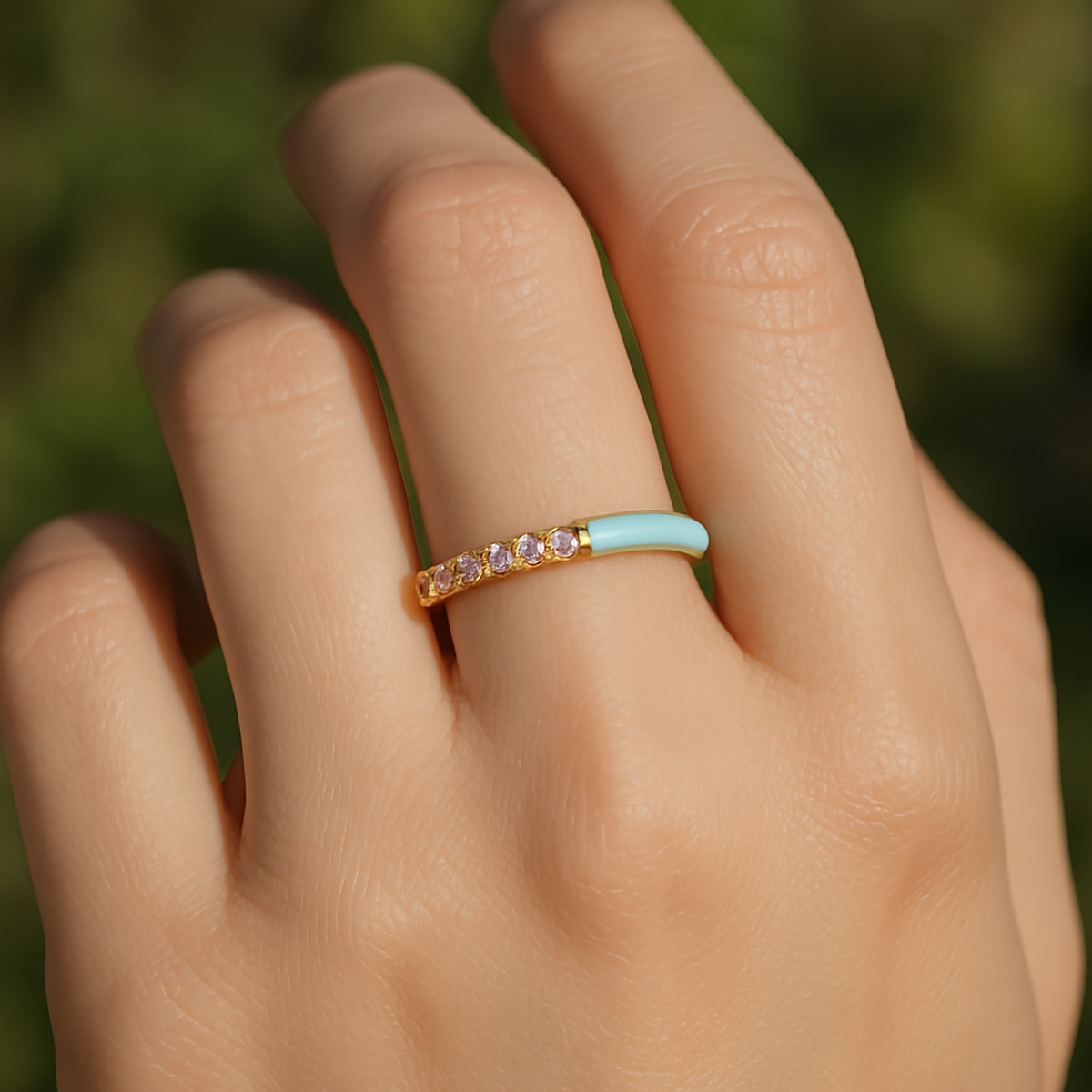 Hand wearing a ring with a turquoise band and small stones against a blurred green background