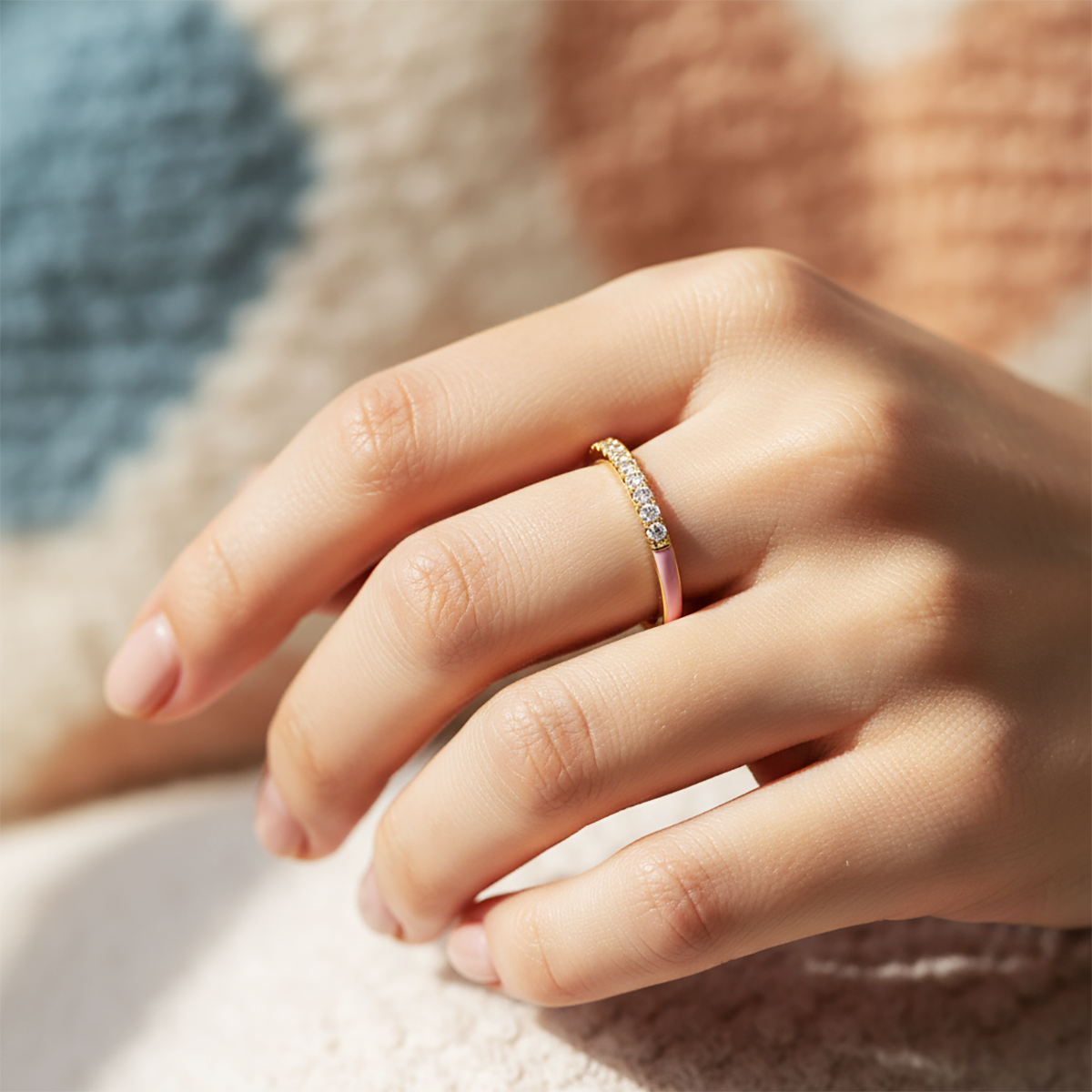 Close-up of a hand wearing a pink ring with a diamond on a soft fabric background