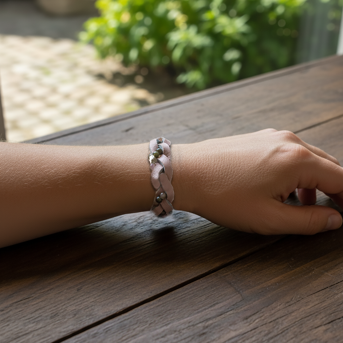 Hand wearing a bracelet on a wooden surface with greenery in the background