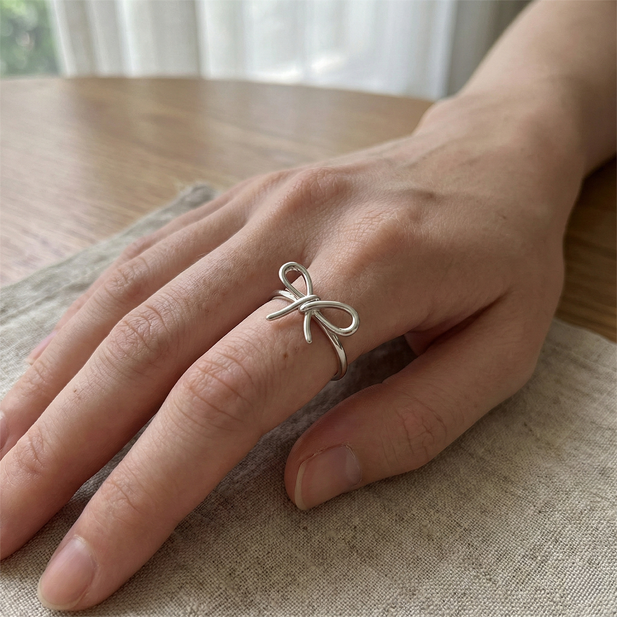 Hand wearing a silver bow-shaped ring on a wooden surface