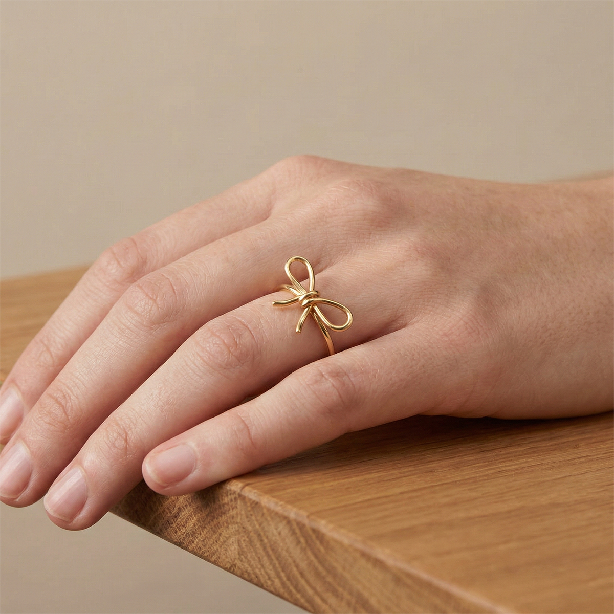 Gold bow-shaped ring on a hand resting on a wooden surface with a beige background