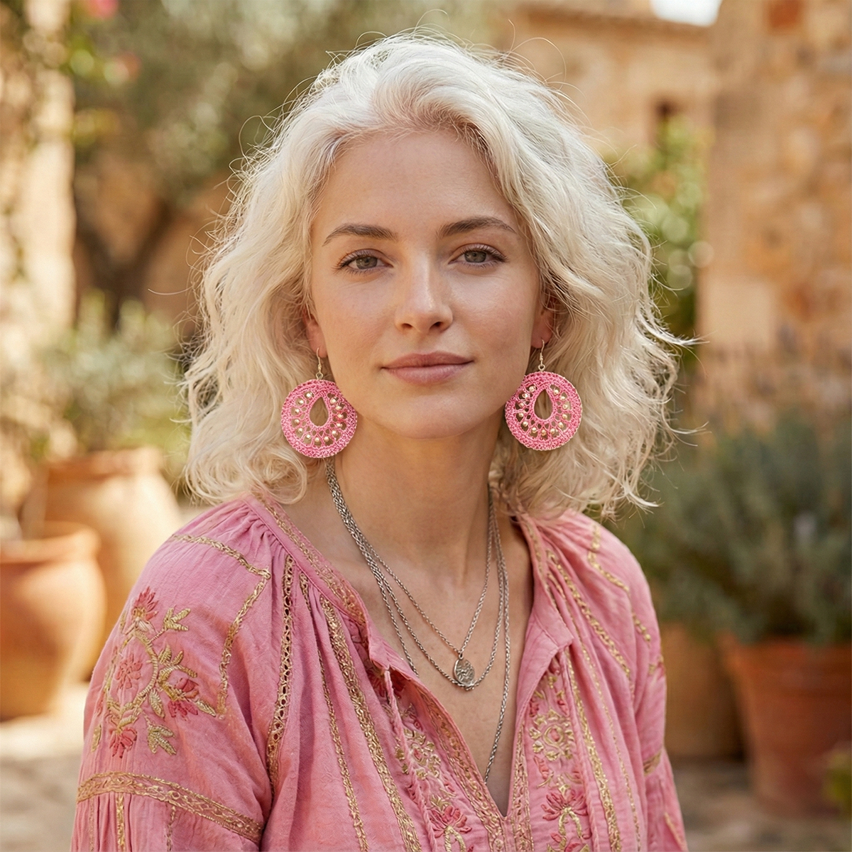 Woman wearing pink earrings and a pink top with floral patterns, standing outdoors.
