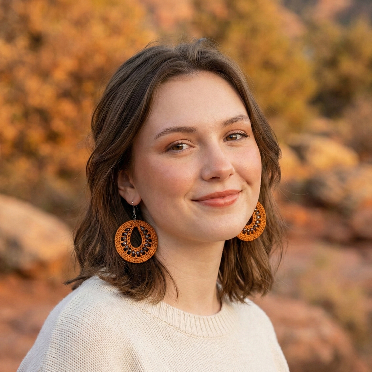 Woman wearing large orange earrings with a blurred natural background