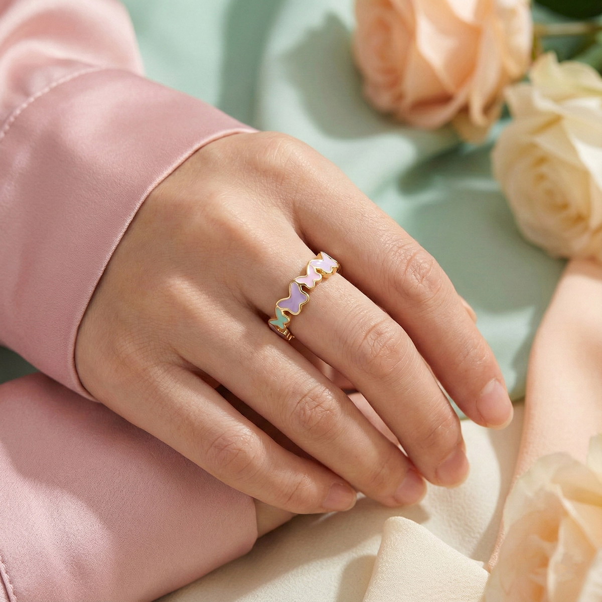 Hand wearing a ring with colorful butterfly charms on a light green background with flowers.