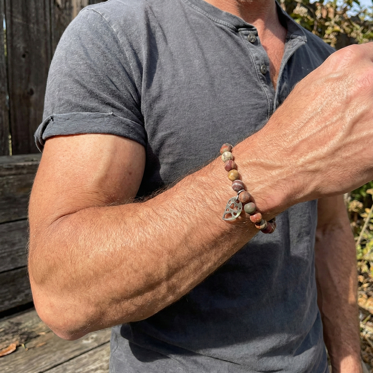 Person wearing a gray shirt with a beaded bracelet on an arm outdoors.