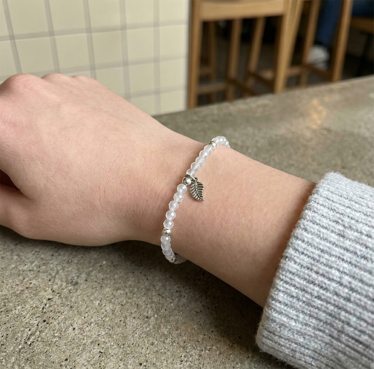 Hand wearing a beaded bracelet with a leaf charm on a neutral background