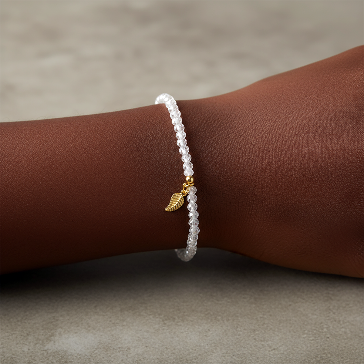bracelet with a gold leaf charm on a wrist against a neutral background
