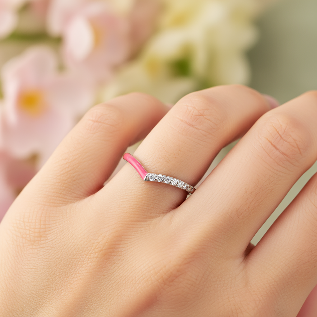 Hand wearing a silver ring with pink band against a blurred floral background