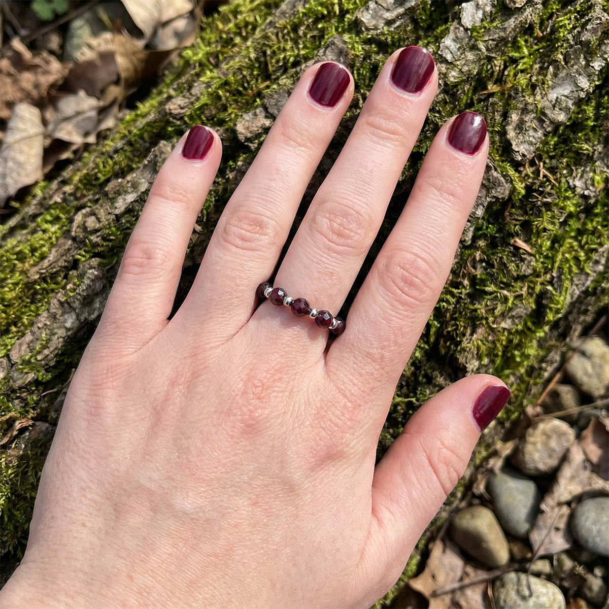 Hand wearing a ring with maroon gemstones against a natural background