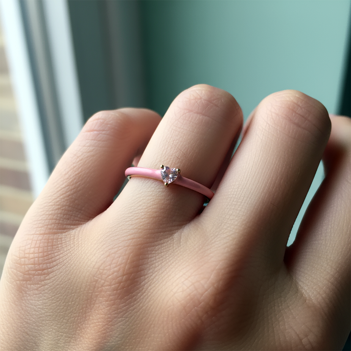 Hand wearing a pink ring with a heart-shaped gemstone against a blurred background