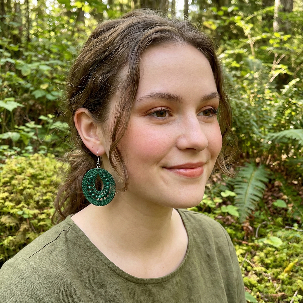 Woman wearing green earrings in a forest setting
