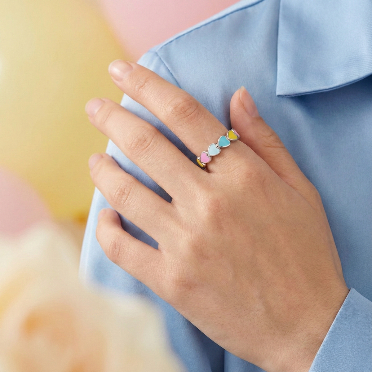 Hand wearing a colorful heart-shaped ring against a blurred background