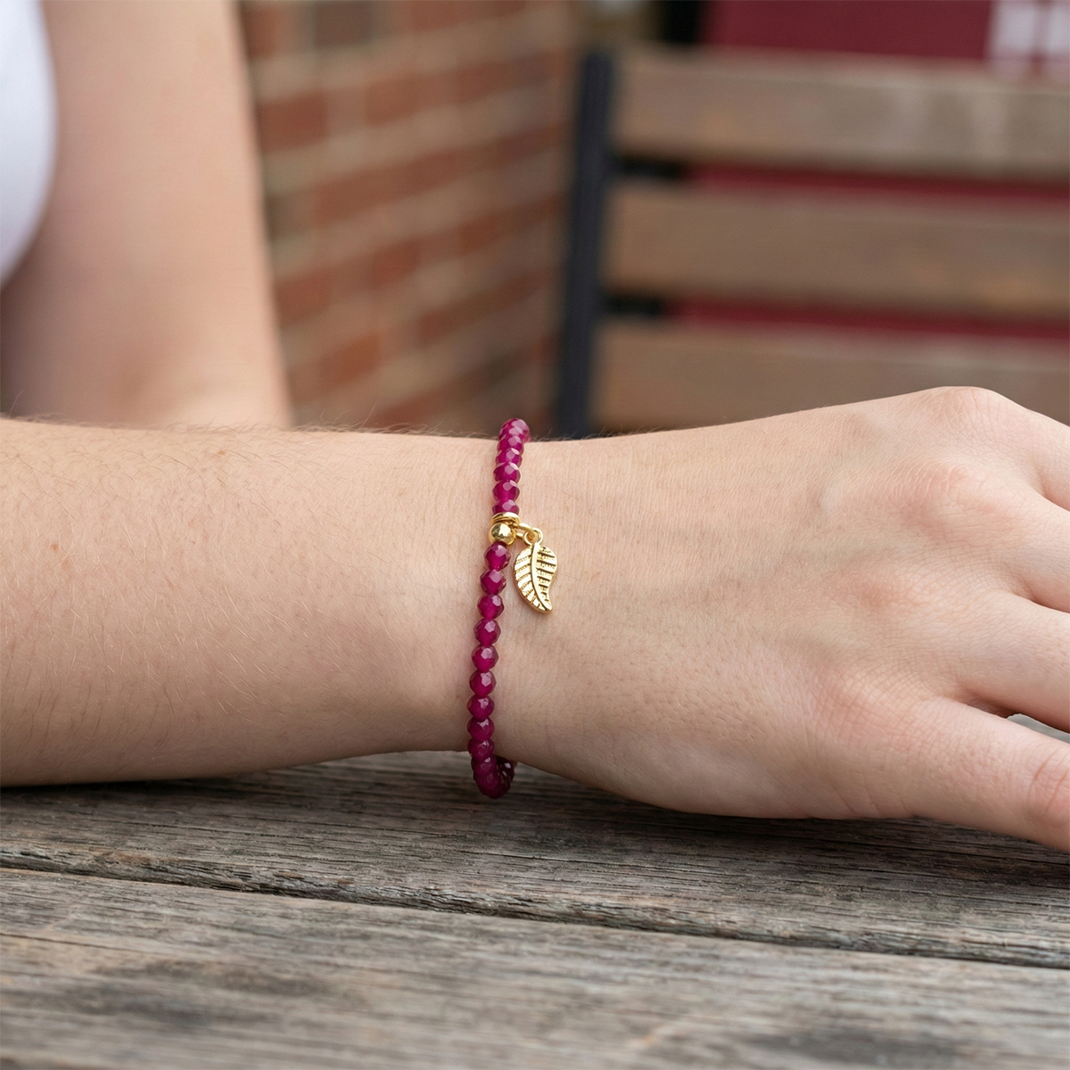 Person wearing a pink beaded bracelet with a gold leaf charm on a wooden surface.