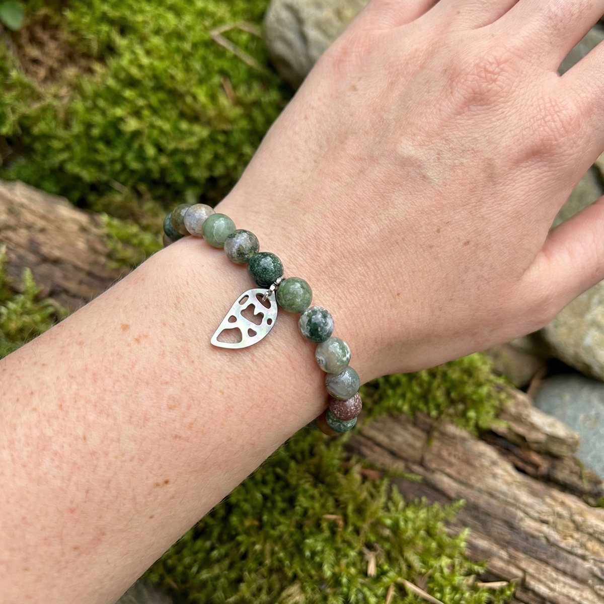 Green beaded bracelet with a silver heart charm on a wrist against a natural background