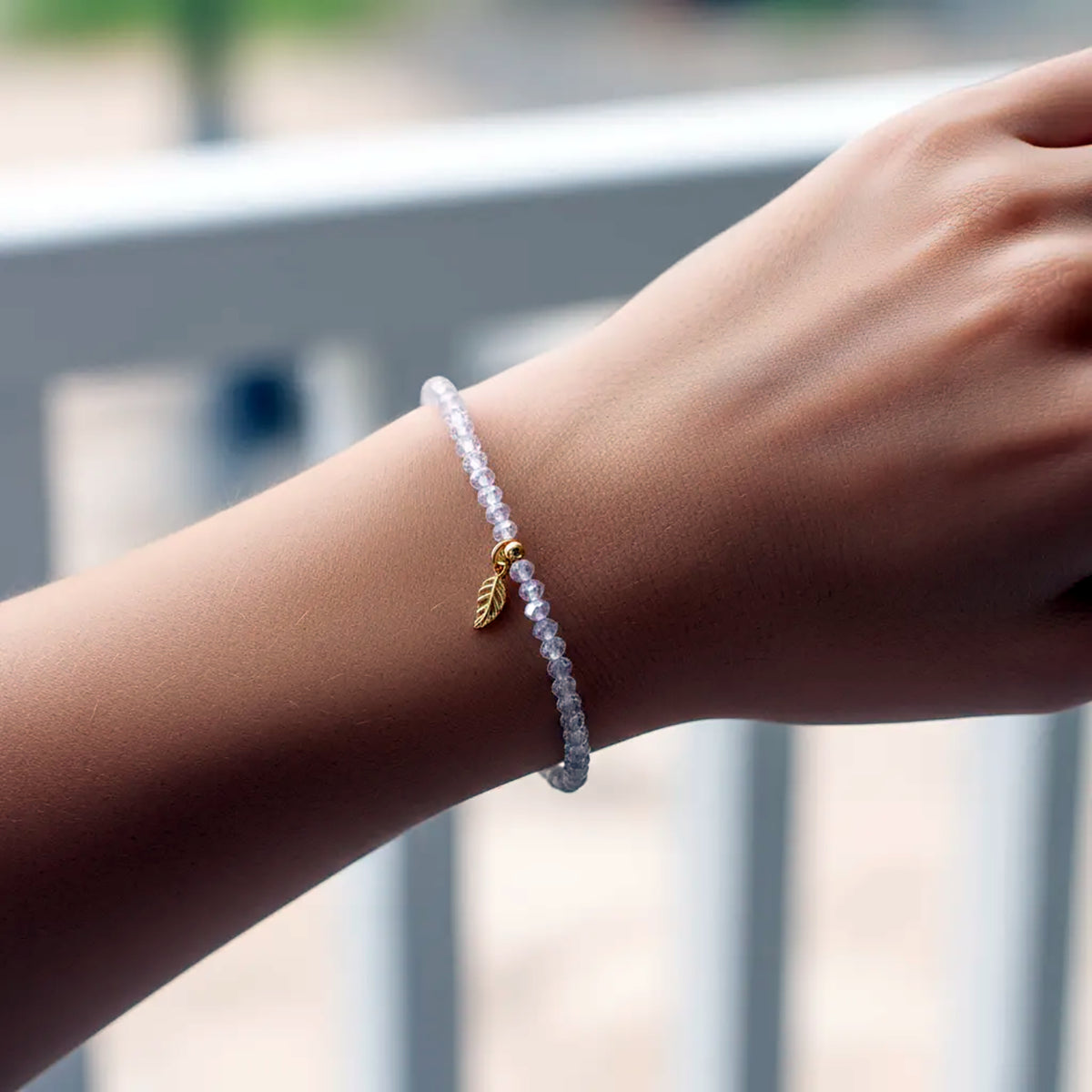 Hand wearing a beaded bracelet with a gold leaf charm against a blurred outdoor background