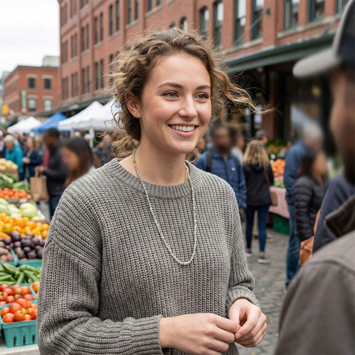 Woman smiling at an outdoor market with people and produce in the background