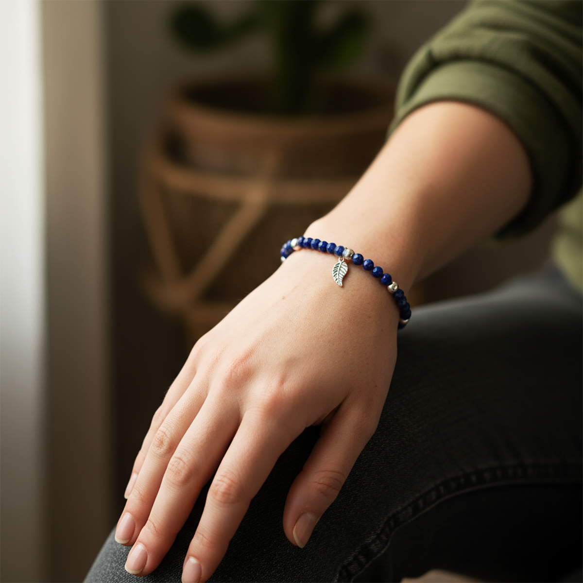 Hand wearing a blue beaded bracelet with a leaf charm, blurred background