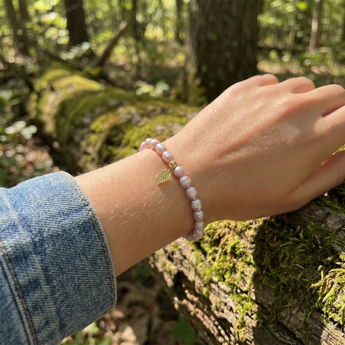 Hand wearing a pink beaded bracelet with a leaf charm against a forest background